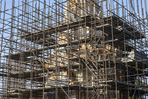 Old ancient temple ruins undergoing restoration process covered with extensive metal scaffolding network under bright clear sky inspiring hope for preservation of beautiful historical architecture