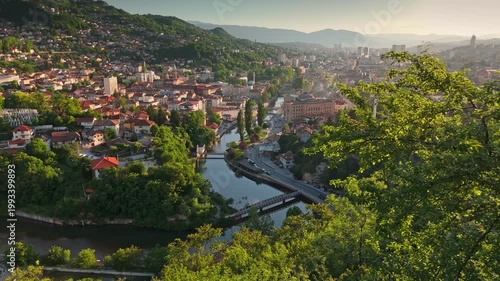 Aerial shot shows the city center of Sarajevo, Bosnia and Herzegovina in a valley. Mountains surround the mix of Ottoman and modern architecture in Sarajevo, Bosnia and Herzegovina
