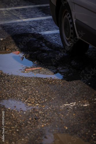 Urban scene with car passing by a big pothole in the asphalt