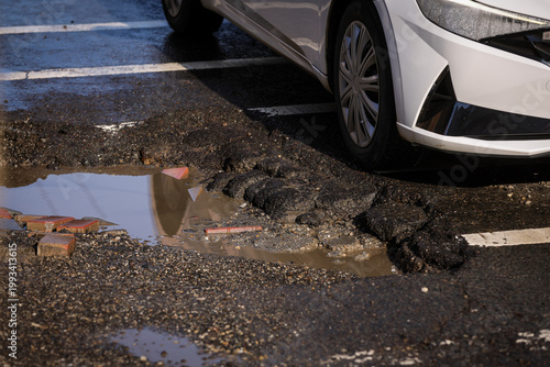 Urban scene with car passing by a big pothole in the asphalt