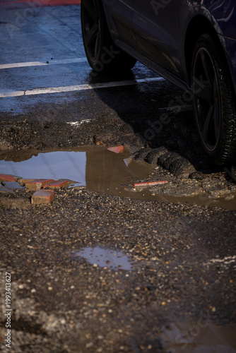 Urban scene with car passing by a big pothole in the asphalt
