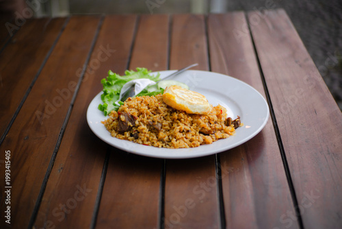Nasi goreng or Indonesian fried rice served with fried egg, cucumber and lettuce on a wooden table in a cafe