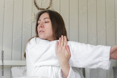 Woman stretching in bed, morning light, soft robe, relaxed expression, cozy white bedding, calm bedroom, waking up before remote work, natural light from the window, quiet moment of self-care. Banner