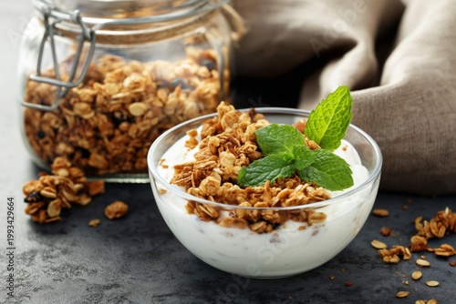 Yogurt With Granola Served in a Clear Bowl With Fresh Mint Next to a Jar of G...