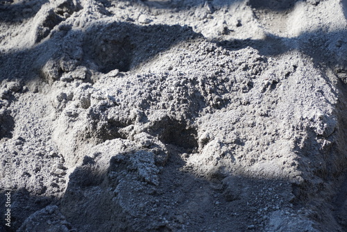 Close up of gray construction sand pile with coarse texture and dramatic shadows. Raw mineral material for building foundation, cement mixing, and industrial masonry work background. Raw Construction 