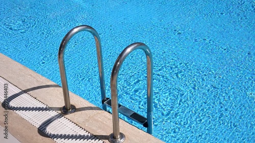 Top view of crystal clear blue water in swimming pool with stainless steel ladder. Professional maintenance, water treatment, luxury resort amenities, summer vacation and relaxation concepts