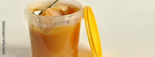 Honey jar banner, single object, isolated. Open plastic bucket, shiny grainy bee honey, golden spoon. Sweet foods industry, honey containers, distribution, beekeeping
