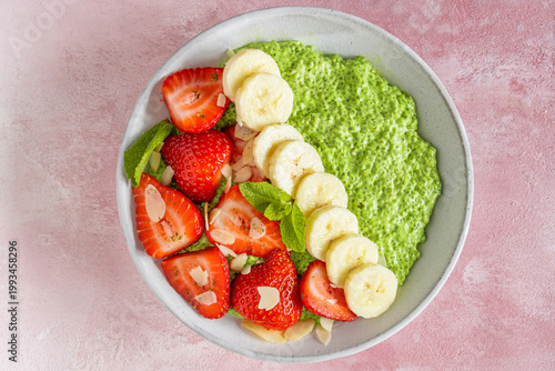 Top view of matcha green tea chia pudding with banana, strawberries and almond flakes in bowl on pink background. Healthy dessert and vegetarian fiber rich breakfast. Flat lay