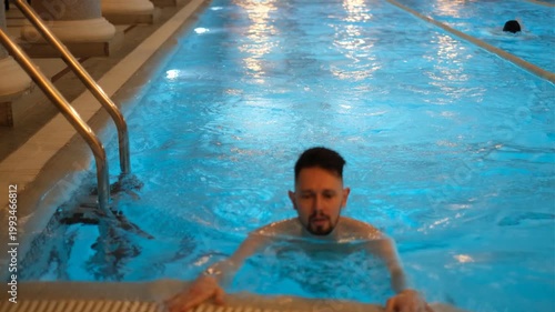 Young dark-haired man swimming in gym pool