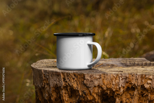 Template of an iron white mug with a black rim on a wood log, on a nature background, outdoors.