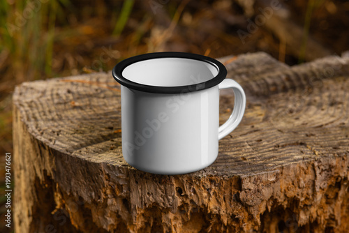Mockup of a white iron mug with a black rim, a handle, on a wood log, on a nature background, outdoors.