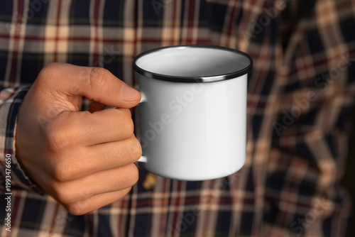 Enamel mug mockup in hand in plaid shirt, empty iron cup for design, print, pattern, branding.