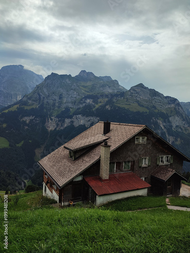 Traditional alpine chalet with mountain peaks and dramatic cloudy sky scenic countryside landscape view