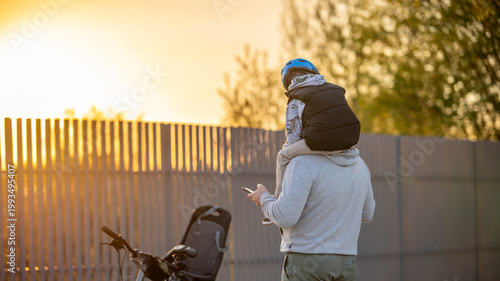 Father carrying little son on shoulders during sunset walk, warm family moment