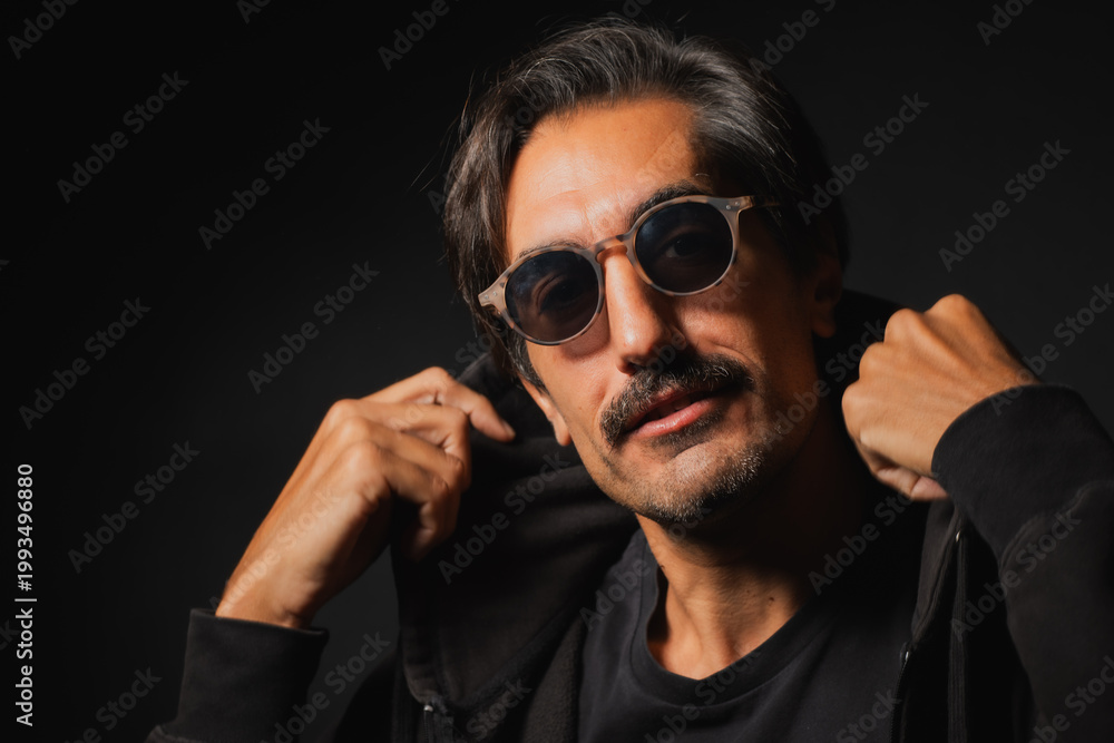 Fototapeta premium Confident man poses stylishly in dark attire and trendy sunglasses