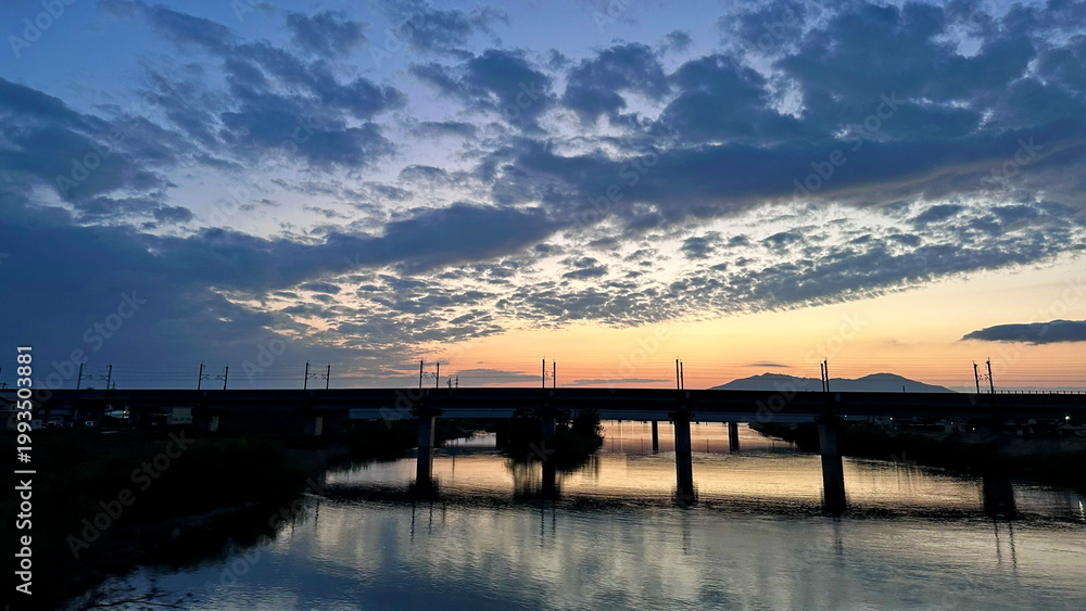 Fototapeta premium Evening view of Nakanokuchi River and railway bridge from Sado Bridge in Tsubame City, Niigata