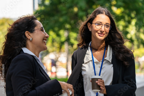 Three businesswomen talking and drinking coffee outdoors, showcasing teamwork, communication, and professional collaboration in a modern corporate environment. Ideal for business, leadership,
