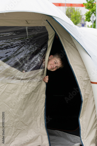 Fotografie a smiling teenage boy peeks his head out from the entrance of a large gray campi