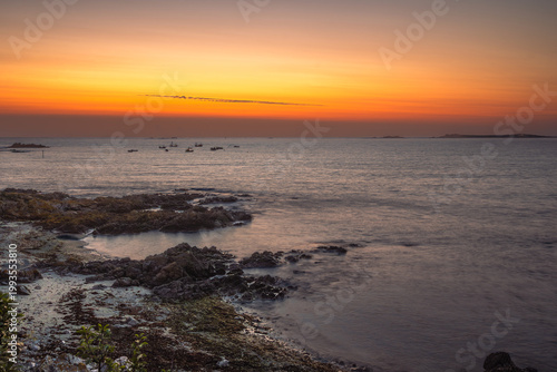 Vibrant sunset over the Atlantic Ocean near Guernsey, Channel Islands, with deep orange and red sky reflecting on calm water.