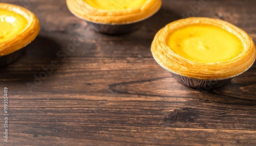 Two golden egg custard tarts with flaky pastry shells sit on a rustic wooden table, showcasing a delicious dessert.