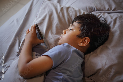 Photos Young boy lying in bed using smartphone while resting on pillow