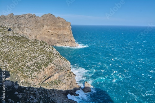 High angle view of the rugged coastal landscape at Cap de Formentor featuring jagged rock formations and white surf crashing against the shoreline.