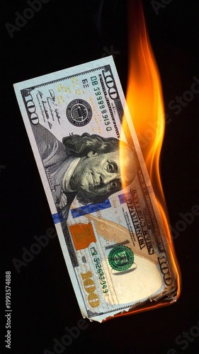 One hundred dollar bill on fire against a black background symbolizing financial loss, inflation and economic crisis
