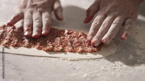 Male hands spreading minced meat on a long flat dough for making a traditional Turkish pide, fa01