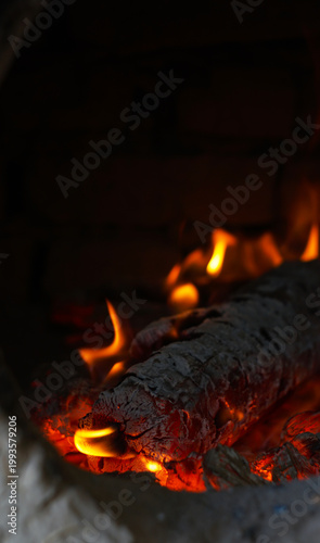 Close-up of a burning log with bright orange flames and glowing embers.