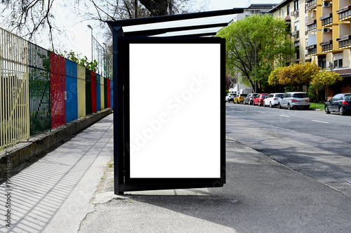 bus shelter at a busstop. blank billboard ad display. empty white lightbox sign. ad space. city transit station. glass structure. urban street setting with parked cars. outdoor advertising concept.