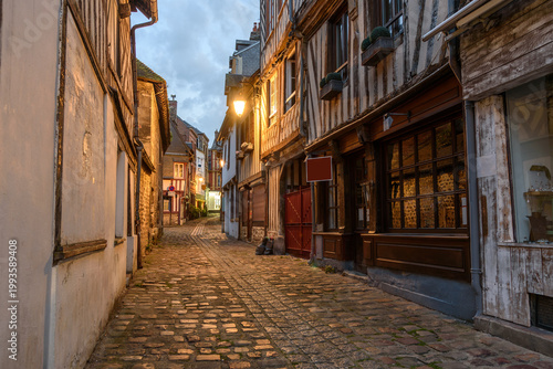 Historic timber framed buildings and shops along a narrrow cobblestone street in a old town at twilight in summer