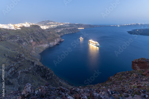 Fotografia A stunning long-exposure twilight view from the Imerovigli cliffs, showcasing glowing cruise ships in the caldera and the sparkling lights of Fira village perched atop the dark volcanic cliffs
