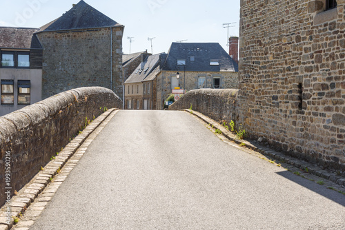 Deserted old stone bridge leading to a historic city centre with traditional stone architecture on a sunny summer day
