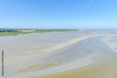View from above of mudflats along the coast of Normandy on a clear summer day.  Agricultural fields are viisible in distance.