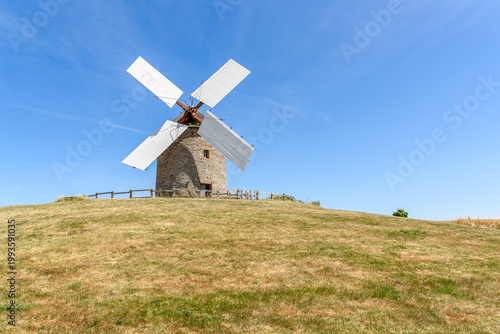 Traditional stone windmill on a grassy hill in the countryside of Normandy on a clear summer day