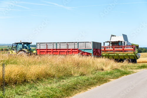Combine harvester and a trailer pulled by a tractor stationary in a field on a clear summer day