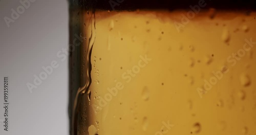 Extreme close-up of a refreshing glass of cold light beer with condensation droplets slowly running down its side, showcasing the beverage's carbonation and crisp, golden color