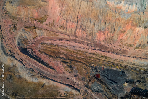Open pit mine with colorful ore layers and industrial transport roads in quarry canyon under bright sunlight, aerial drone shot