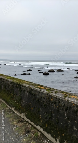Coastal Seascape with Stone Wall and Overcast Sky, Serene Ocean View.