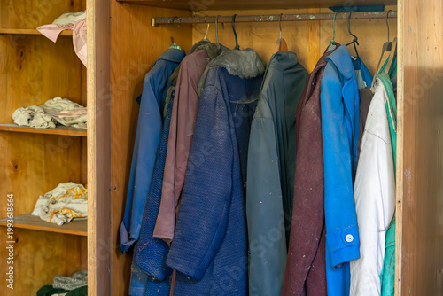 Photography Old wooden wardrobe filled with vintage coats and clothing in a dusty interior, concept of nostalgia and decay, rustic room decor, closeup of clothing storage in an old abandoned home