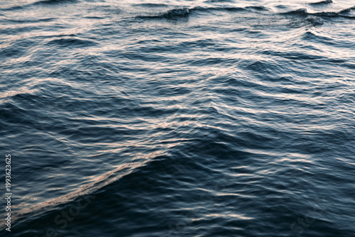 Calm ocean waves under soft evening sunlight, creating serene and peaceful atmosphere. Blur motion of water, gentle rippling of the sea with sunset light reflections. Aesthetic slow living concept.
