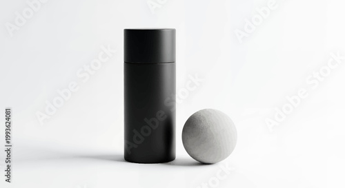 Black cylindrical container and gray stone sphere on white background