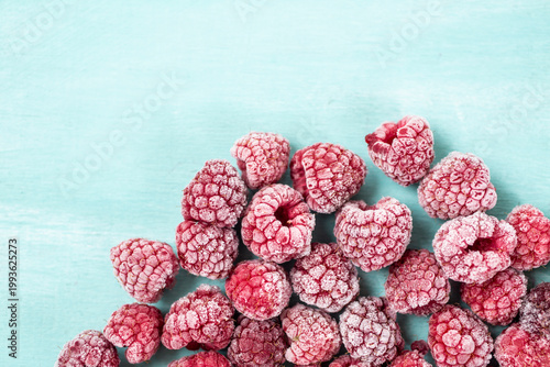 A pile of frozen raspberries covered with frost is scattered on a light blue background.