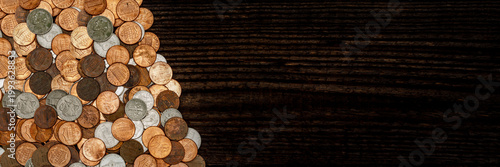 Coins are arranged in a pile on a dark wooden surface showing different denominations and sizes of currency