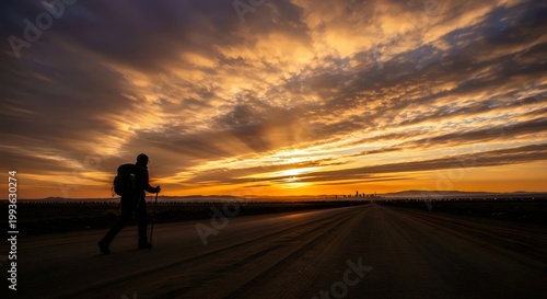 Golden hour scene with lone figure walking on dusty trail beneath glowing orange sky