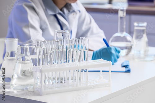 Glassware with water samples against female scientist working at table in lab...