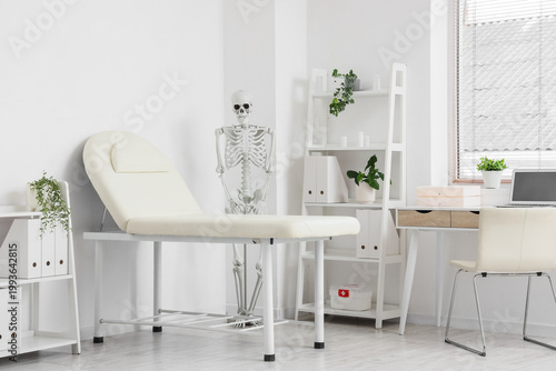 Interior of medical office with human skeleton model, couch and workplace