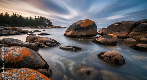 Serene coastal landscape with smooth boulders, orange lichen, and long exposure misty water at sunset
