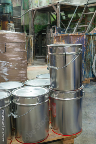 Chemical storage in a manufacturing plant with signs of recent use and logistical preparation. Sealed paint containers and stacked boxes in a production facility interior
