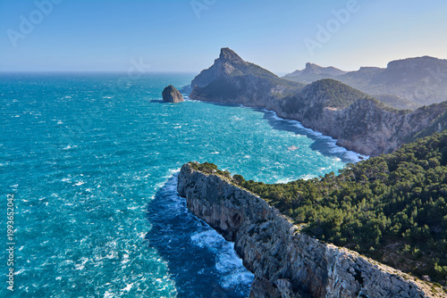 Dramatic panoramic landscape of the rugged northern coast of Mallorca showcasing steep limestone cliffs and dense pine forests meeting the vibrant blue sea.